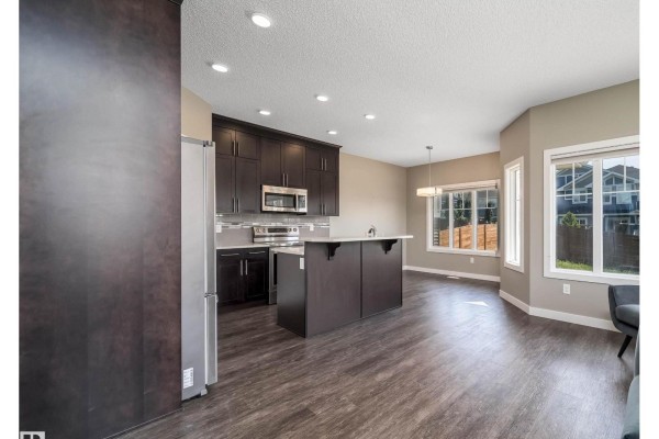 Open concept kitchen with dark wood cabinets, white island, and dining area. - 114 James Cr, St  Albert