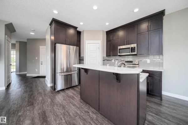 Kitchen with dark wood cabinets, stainless steel appliances, and island with white countertop. - 114 James Cr, St  Albert
