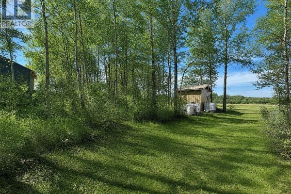 View of the property with leafless trees, a wooden shed, and water tanks on dry grass. - 114 James Street, Good Spirit Lake