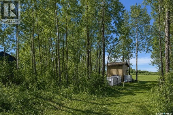 Trees and brush surround a small shed and some water tanks on a sunny day with clouds. - 114 James Street, Good Spirit Lake