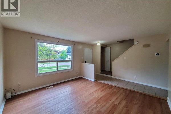 Living room with wood-look laminate flooring, beige walls, and a large window overlooking the front yard. - 114 Lillian Drive Unit# B, Waterloo