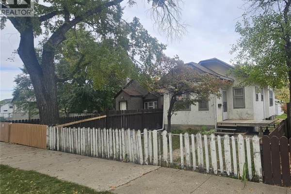 Exterior of the house showing the front and side with mature trees and fences. - 114 N Avenue S, Saskatoon