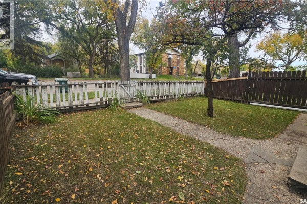 Looking across the grassy yard towards the street with houses and trees in the background. - 114 N Avenue S, Saskatoon