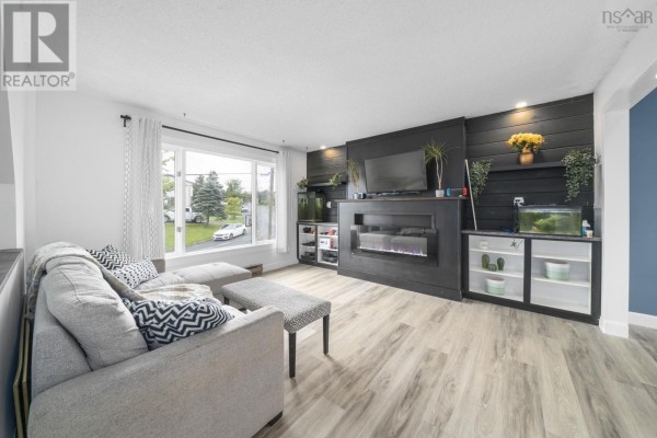 Living room with gray sectional sofa, ottoman, fireplace, and large window overlooking the front yard. - 114 Romkey Drive, Eastern Passage