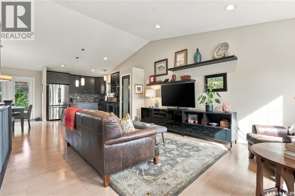Living room with leather sofa, rug, and view of kitchen with dark cabinets. - 114 Senick Crescent, Saskatoon