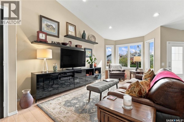 Living room featuring brown leather sofa, armchair, media console, and large windows. - 114 Senick Crescent, Saskatoon