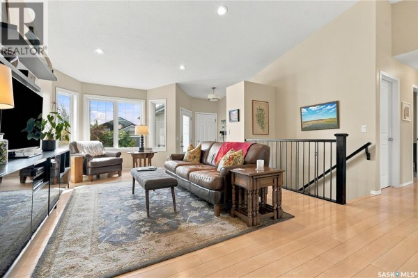 Living room with vaulted ceiling, hardwood floors, leather sofa, and staircase railing. - 114 Senick Crescent, Saskatoon