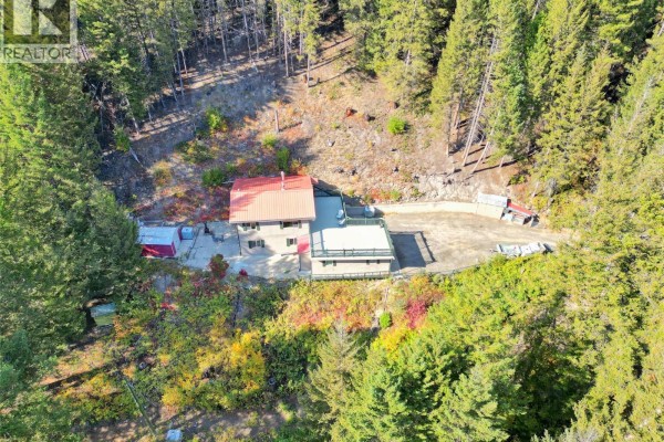 Aerial view of a house with a red roof, garage, and deck, situated on a wooded slope with surrounding greenery. - 114 Thistle Road, Princeton