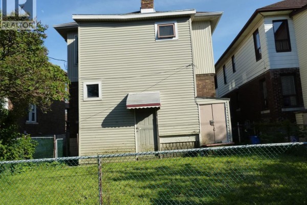 Rear view of a duplex with light-colored siding, showing a small door, shed, and chimney. - 1140 Giles Boulevard East, Windsor
