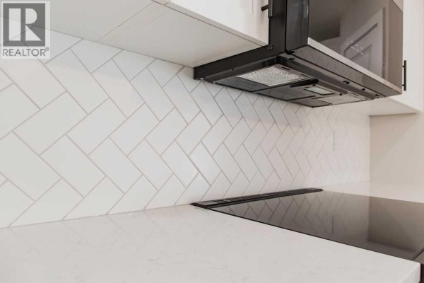 White kitchen with stainless steel appliances, quartz countertops, and light wood laminate flooring. - 11407 95 Street, Clairmont