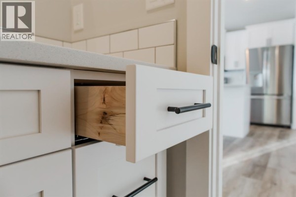 Close-up of white kitchen cabinets, stainless steel appliances, and open drawer. - 11416 95 Street, Clairmont