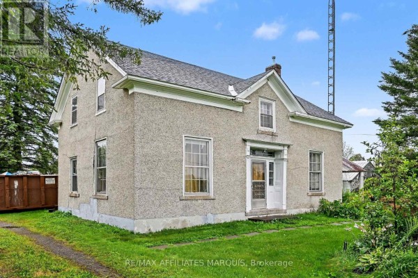 Three-quarter view of the farmhouse exterior with a metal bin on the left lawn. - 11422 7th Line Road, Elizabethtown Kitley
