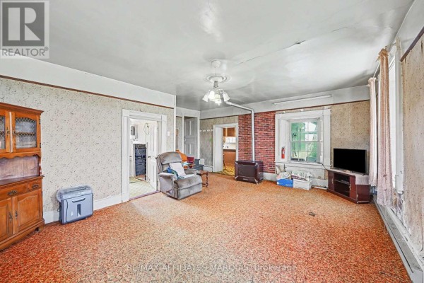 Living room with orange patterned carpet, a recliner, a television, and a brick fireplace. - 11422 7th Line Road, Elizabethtown Kitley