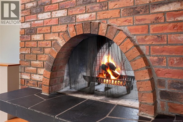 Close-up of a brick fireplace with a metal screen and burning logs. - 1144 May St, Victoria