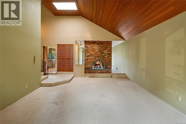 Spacious living room with vaulted wood ceiling, brick fireplace, and light green walls. - 1144 May St, Victoria