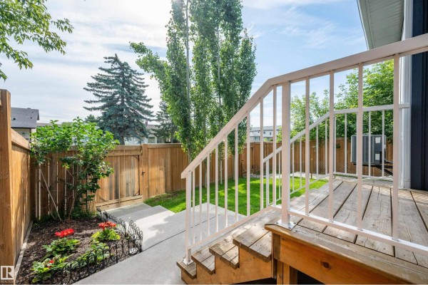 View from a wooden deck down into a fenced backyard with green grass and garden beds. - 11444 82 St Nw, Edmonton