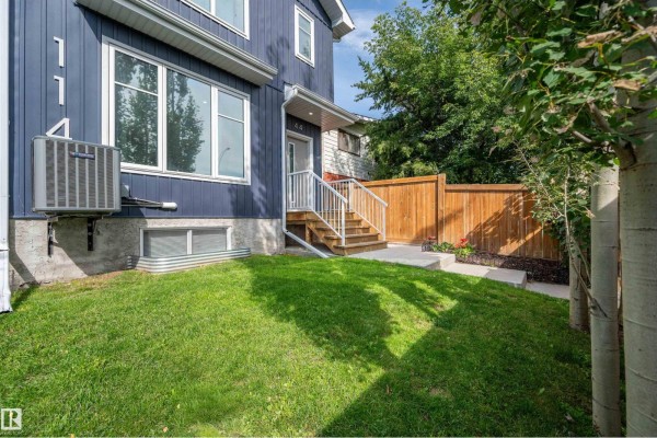 Side view of the blue duplex exterior showing a window, air conditioning unit, and grassy lawn. - 11444 82 St Nw, Edmonton