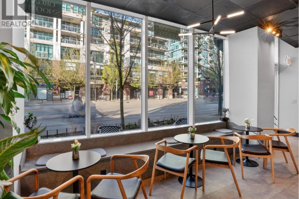 Modern cafe interior with multiple tables, chairs, and expansive windows facing an urban streetscape. - 11450 Confidential, North Vancouver