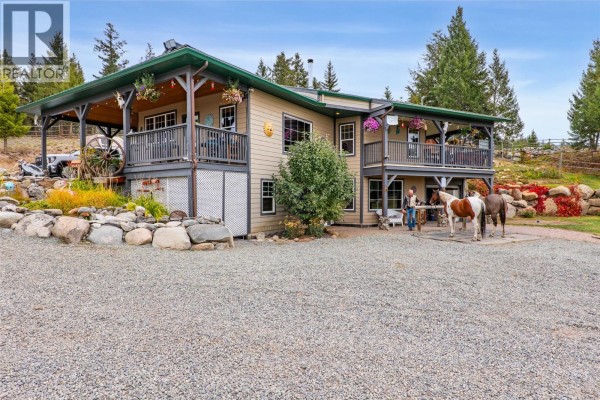 Side view of the house showing a wraparound deck with two horses standing nearby. - 11460 Hwy 97c Highway, Merritt
