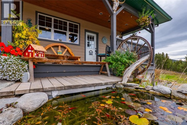 Close-up of the front porch with a wooden bench, decorative wheels, and a fish pond. - 11460 Hwy 97c Highway, Merritt
