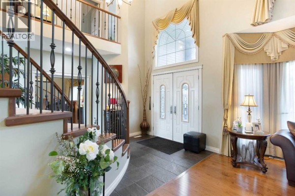 Front entryway with double doors, arched window, curved staircase, and dark tile flooring. - 1149 Channelside Drive Sw, Airdrie