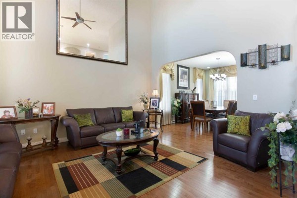 Spacious living room with vaulted ceiling, large mirror, brown leather sofas, and hardwood floors. - 1149 Channelside Drive Sw, Airdrie