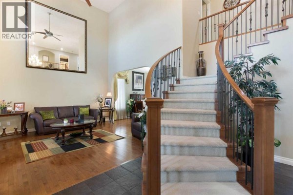 Curved carpeted staircase with wooden banister and black spindles in a large, open foyer. - 1149 Channelside Drive Sw, Airdrie