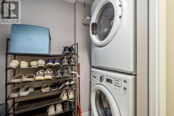 Laundry room with stacked white washer and dryer and a shoe rack. - 115, 10 Kincora Glen Park Nw, Calgary
