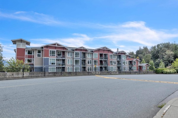 Modern white kitchen with stainless steel appliances and island seating for four people. - 115 2242 Whatcom Road, Abbotsford