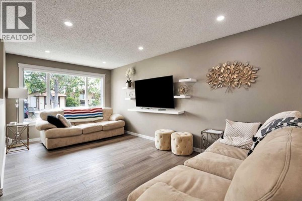 Living room with beige sectional sofa, television, ottomans, and large window. - 115 Abingdon Crescent Ne, Calgary