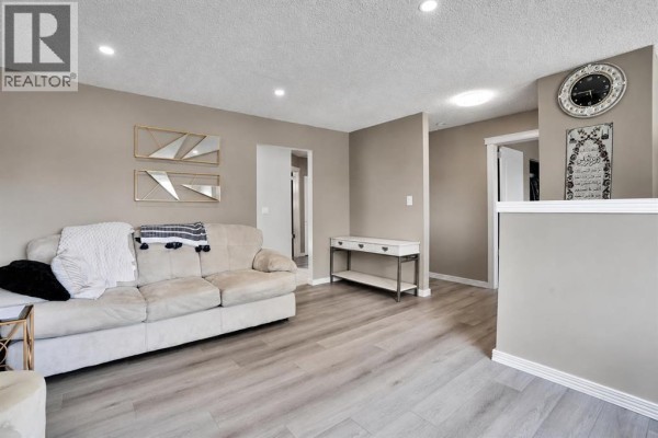 Living room with beige sofa, console table, clock, and doorway views. - 115 Abingdon Crescent Ne, Calgary