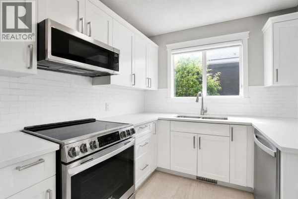 Modern kitchen with white cabinets, stainless steel appliances, quartz countertops, and subway tile backsplash. - 115 Abingdon Crescent Ne, Calgary