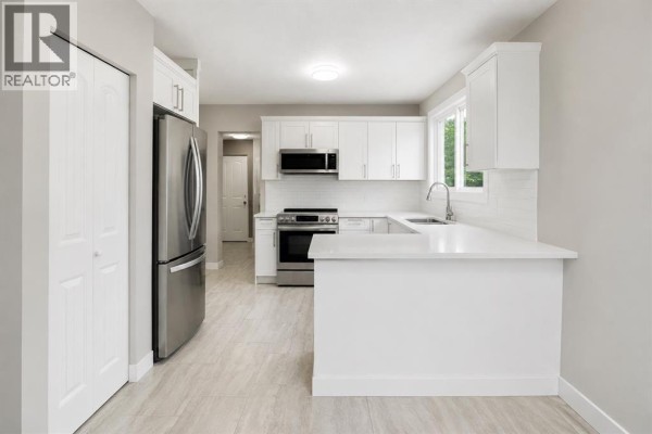 U-shaped kitchen with white cabinets, stainless steel appliances, quartz countertops, and pantry door. - 115 Abingdon Crescent Ne, Calgary