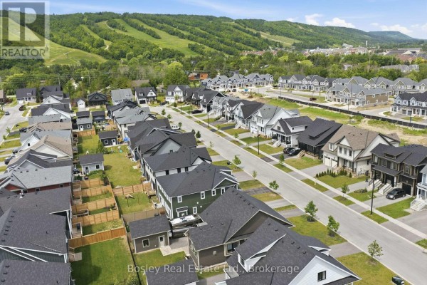 Aerial view of a street lined with houses, some with garages, facing a wooded hill. - 115 Black Willow Crescent, Blue Mountains