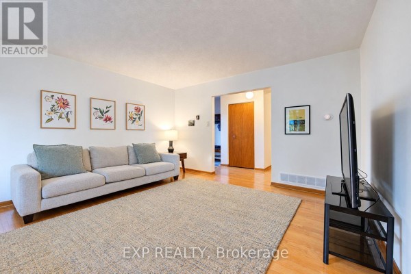Living room with two neutral sofas, a large rug, bay window, and wooden floors. - 115 Chopin Drive, Kitchener