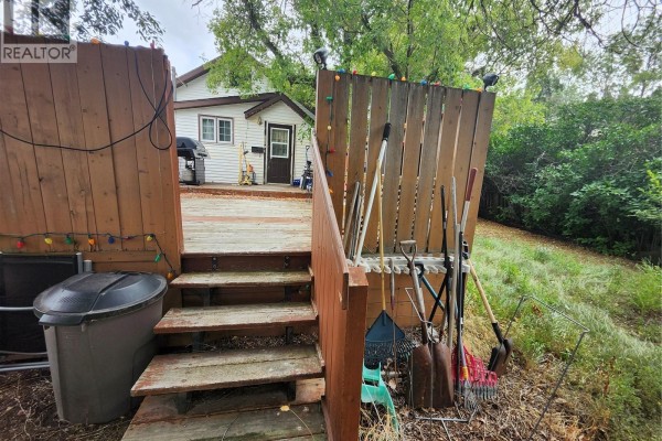 Wooden steps leading up to a deck with gardening tools leaning against a fence. - 115 Halyard Street, Pennant