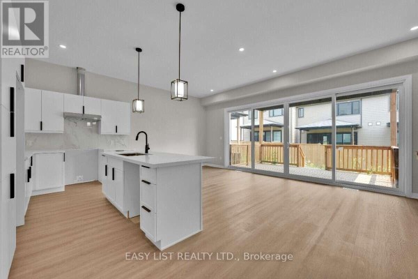 Open-concept kitchen and living area with white cabinets, island, and patio doors to a deck. - 115 Ivy Crescent, Thorold
