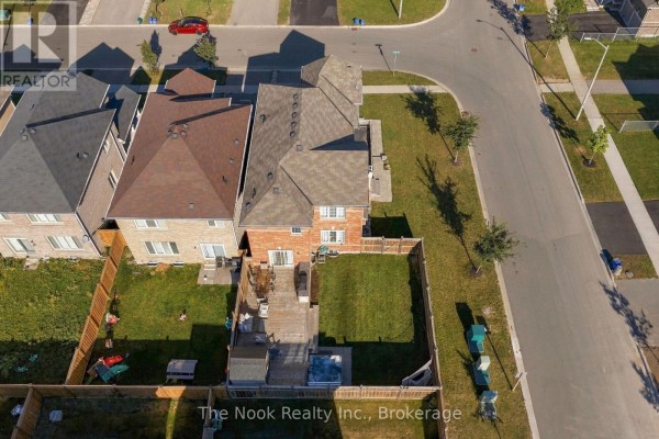 Aerial view of the backyard of a red brick house with a wooden deck, hot tub, and green lawn. - 115 Noden Crescent, Clarington