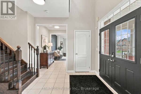 Interior foyer with beige tile flooring, dark wood staircase, white doors, and a view into the living room. - 115 Noden Crescent, Clarington