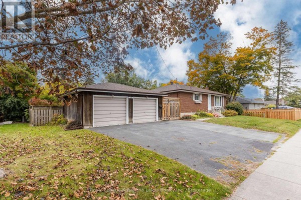 Driveway and detached two-car garage with light brown doors on a cloudy day with fall leaves. - 115 Victoria Avenue N, Kawartha Lakes