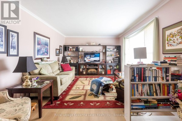 Living room with a beige sofa, armchair, large rug, built-in entertainment unit, and bookshelves. - 115 Victoria Avenue N, Kawartha Lakes