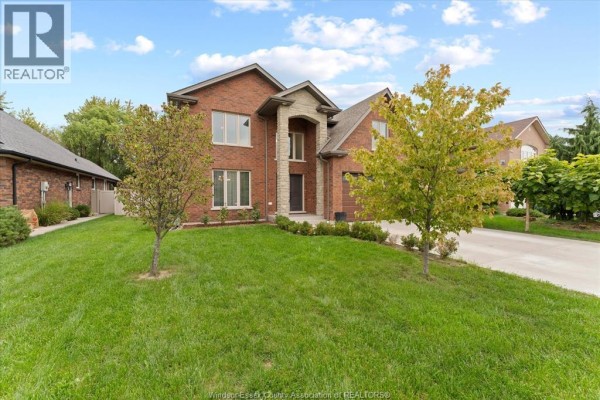 Exterior view of a brick house with a green lawn, mature trees, and concrete driveway. - 1150 Jillian Court, Lakeshore