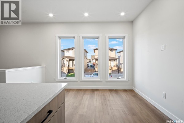 Living area with three windows and wood laminate flooring. - 1150 Poley Street N, Regina