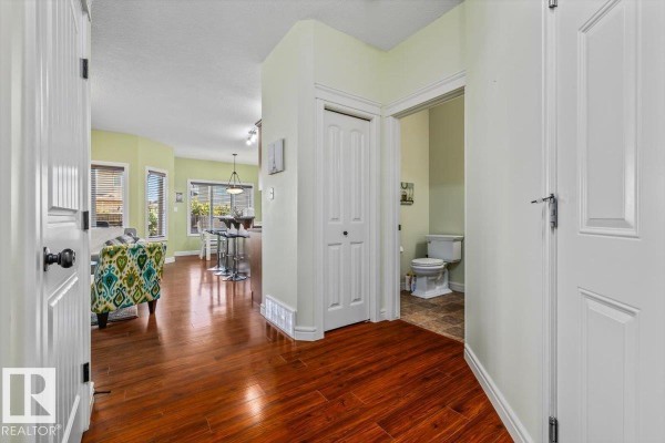 View from the hallway into a powder room with a toilet and the living area beyond. - 11506 17 Av Sw, Edmonton