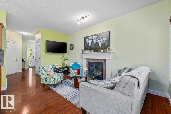 Living room with a grey sofa, patterned chairs, fireplace, and wood flooring. - 11506 17 Av Sw, Edmonton