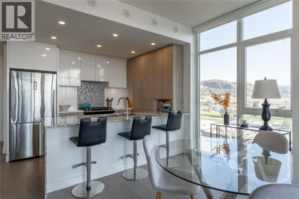 Modern kitchen with white cabinetry, granite countertops, stainless steel appliances, and breakfast bar seating. - 1151 Sunset Drive Unit# 1305, Kelowna