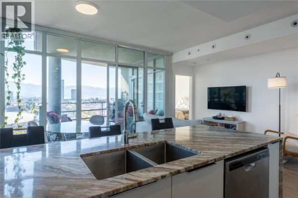 Kitchen island with granite countertop and double sink, overlooking the living area and balcony. - 1151 Sunset Drive Unit# 1305, Kelowna