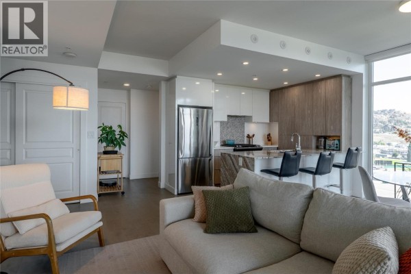 Open concept living and kitchen area with neutral furniture, featuring a sofa, armchair, and kitchen island. - 1151 Sunset Drive Unit# 1305, Kelowna
