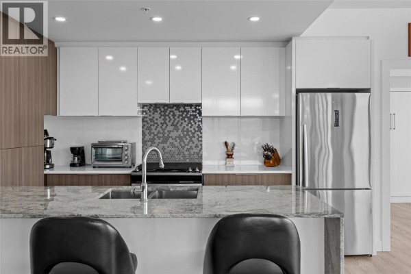 Close-up of the kitchen island with a sink, stovetop, and stainless steel refrigerator. - 1151 Sunset Drive Unit# 1504, Kelowna