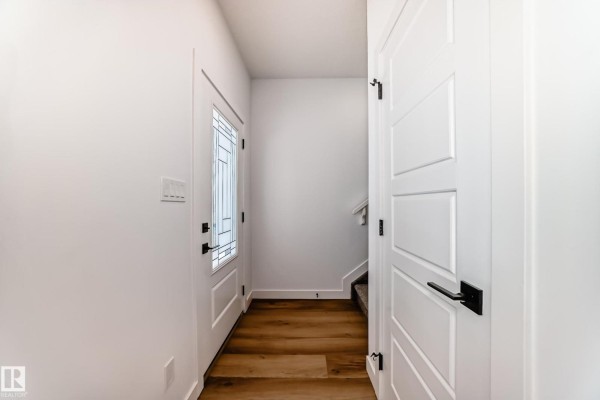 Interior view of a bright hallway with white walls, a glass-paneled front door, and wood-look flooring. - 11519 & 11521 67 St Nw, Edmonton